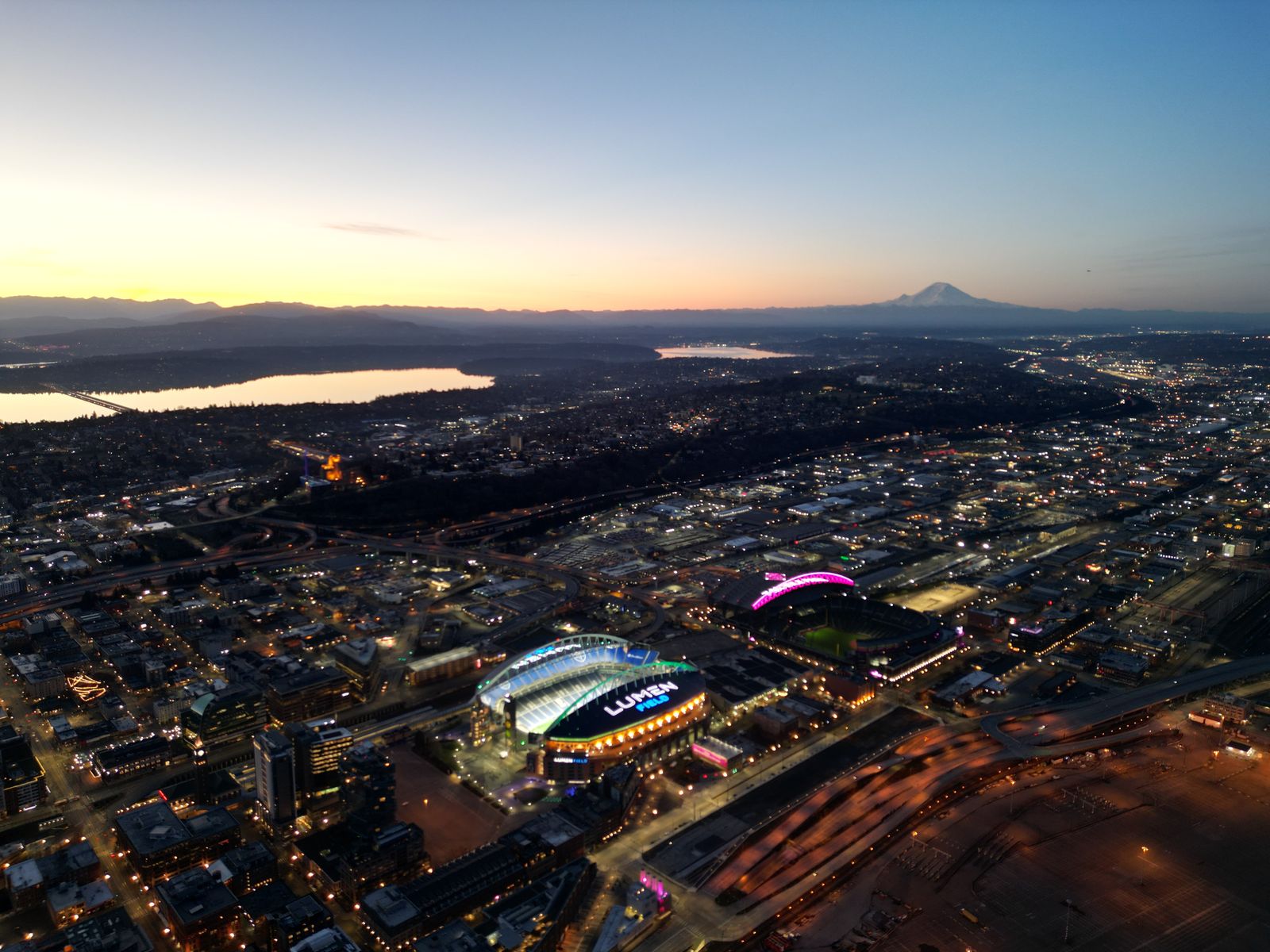 Aerial photograph at dawn looking south over Seattle, the arena lit below and Mount Rainier on the horizon
